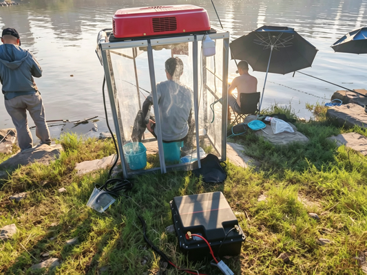 Viral shore fishing setup, angler in homemade air‑condition shelter powered by large deep‑cycle LiFePO4 battery on river bank